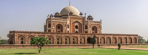 A long ornate building stands against the horizon. The building is orange and white with a large white dome and lots of arches