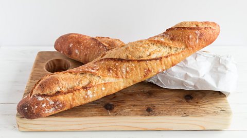 Two baguettes crossing on a chopping board.