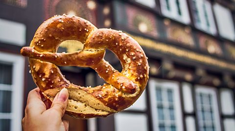 A hand holding up a pretzel against a blurry street backdrop.