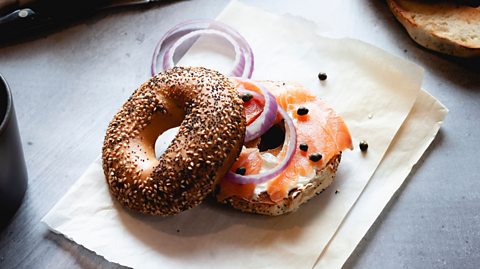 A seeded bagel balanced on another bagel half topped with salmon and red onion slices.