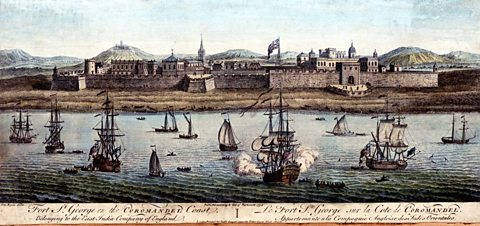 An old colour illustration of a long fort structure stretched out along the bank of a body of water, in front of it, many ships are sailing in the water.