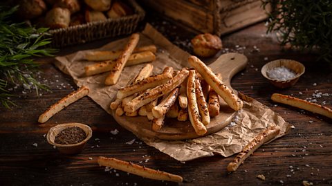 A pile of breadsticks on a chopping board.