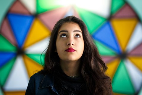 A young woman in front of stained glass windows in a Christian church.