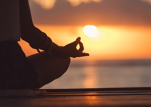 A person meditating at sunset.