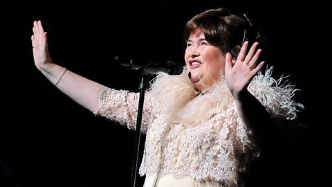 Scottish singer Susan Boyle performing on stage wearing a white, feathered jacket.