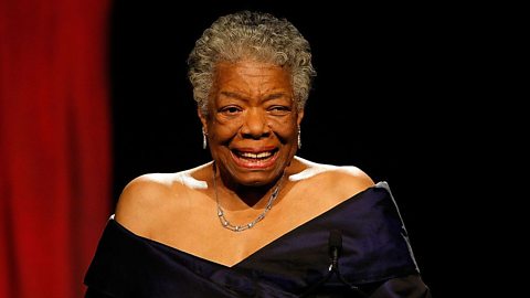 American poet, writer and performer Maya Angelou stands on a stage wearing a black evening gown