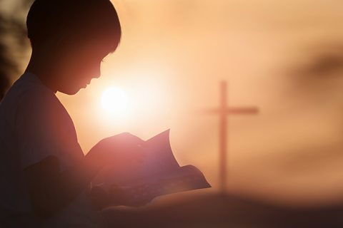 A child reads a Bible with a cross in the background.