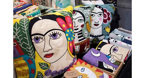 A photo showing four very colourful cushions with Kahlo's face on them, and cushion covers lined up in front of them.