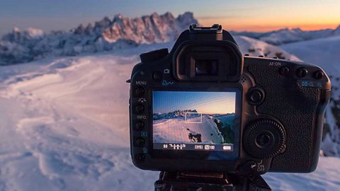 A camera on a tripod. View of a snowy scene in the camera's screen