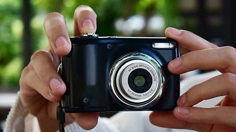 Hands holding a compact camera with the finger on the button