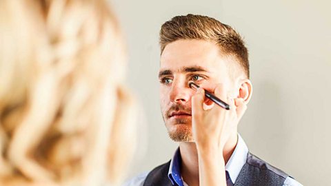 A woman applying makeup to a man's face with a brush