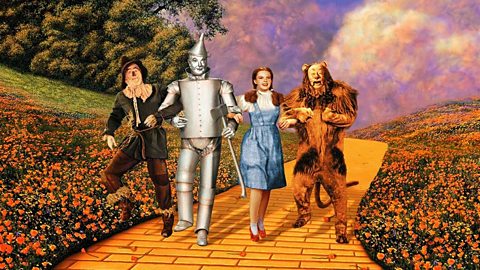 Dorothy, Scarecrow, Tin Man and Lion linking arms on the Yellow Brick Road