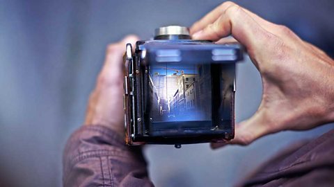 Hands holding a camera with a view of a city street in its screen.