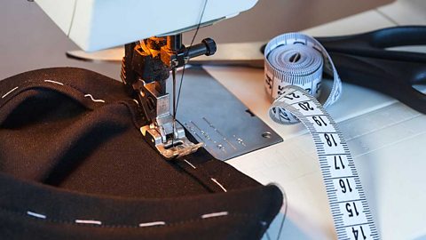 A sewing machine with a piece of black fabric being sewn along a seam