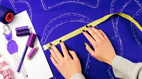 Hands holding a tape measure against blue fabric with designs drawn in chalk.