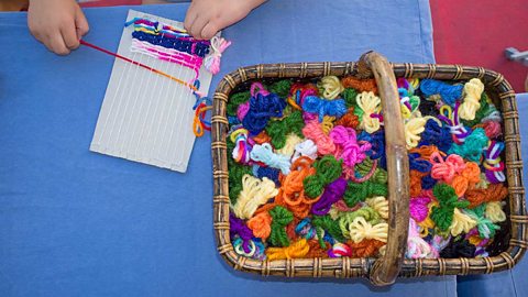 A child weaving with a simple cardboard loom. A basket of coloured yarn