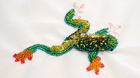 A frog design made of sequins and beads embellishing white fabric