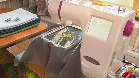 A yellow pattern being embroidered into blue cloth by a sewing machine