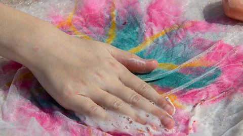 Hands washing fabric and felt in soapy water