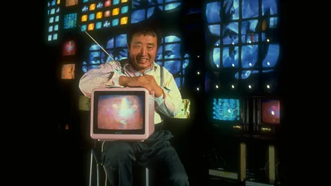 Mario Ruiz/ Getty US-Korean artist Nam June Paik, shown here with his 1989 video sculpture Fin de Siecle II, was an early adopter of video art (Credit: Mario Ruiz/ Getty)