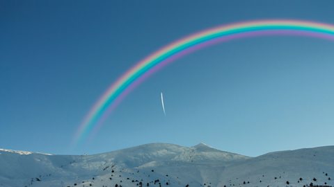 A rainbow over a snowy mountain top.