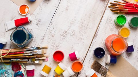 Lots of different paintbrushes and pots of different paints. 