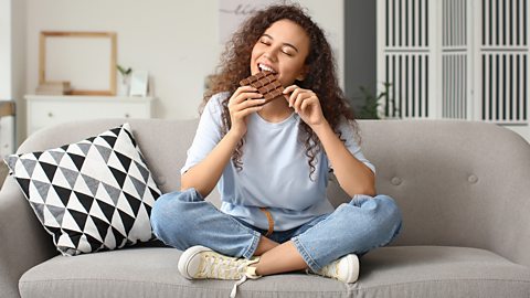 A person sits on the sofa eating chocolate