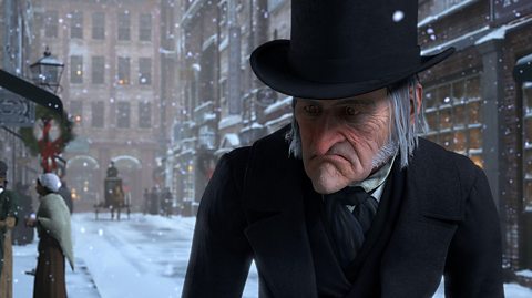 Scrooge, played by Jim Carrey, from the 2009 Disney animated film version. Scrooge wears a black top hat and black coat. He is scowling and has grey hair and stubble. He is walking down a Victorian street and it is snowing,