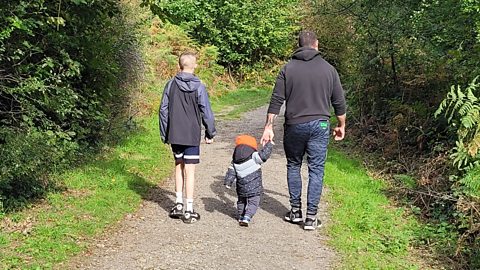 A dad taking his two children on a walk through the forest