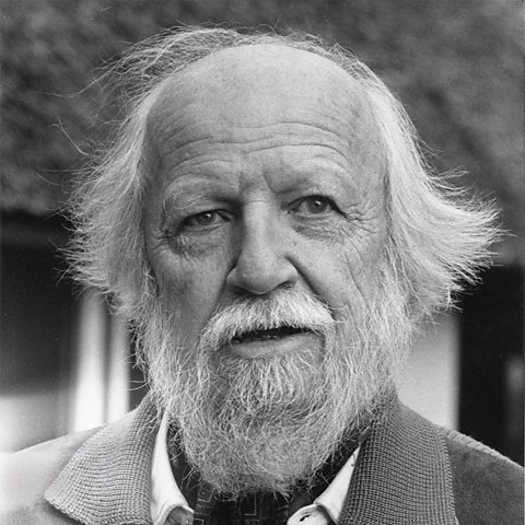 A black a white photograph of William Golding. He has white hair and a beard and is wearing a smart jacket.