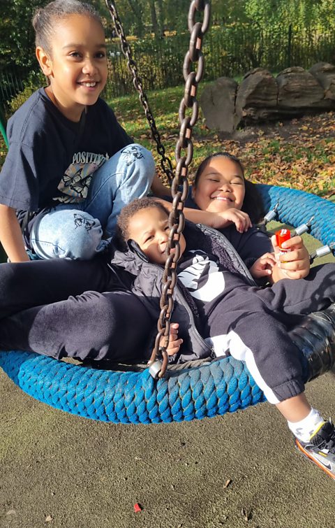 Two girls and a baby boy playing in a nest swing in a park