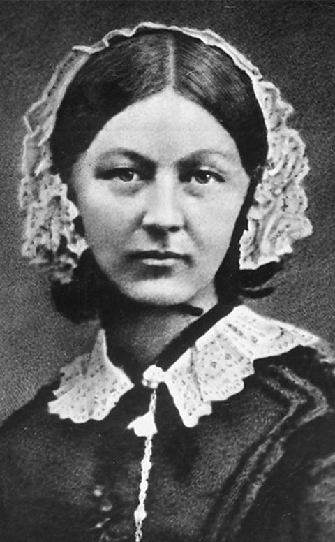 A black and white portrait photograph of Florence Nightingale. She wears a white lace bonnet partially covering her hair which falls just past her chin. Her dark dress has a white lace collar. 