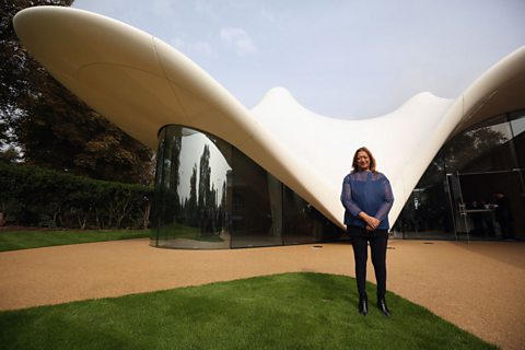 Zaha Hadid wearing a blue top, standing in front of the Serpentine Sackler Gallery in London in 2013, which she designed