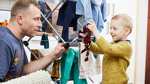 A dad and his son playing with laundry on a clothes horse.