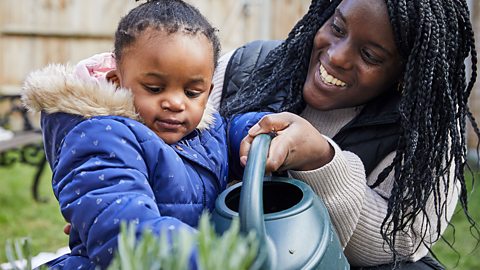 A mum and her toddler daughter watering the plants with a watering can.