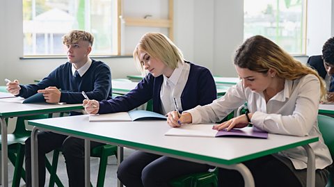 Three school students in uniform study for a test with their exercise books in a classroom