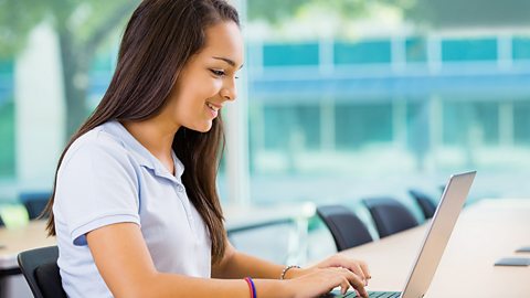 A school student sits in a classroom and works on her laptop