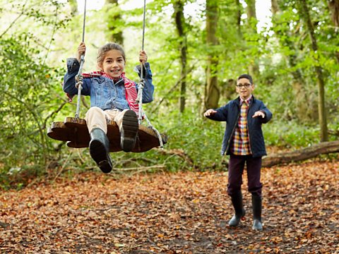 A girl on a swing with a boy standing behind her.