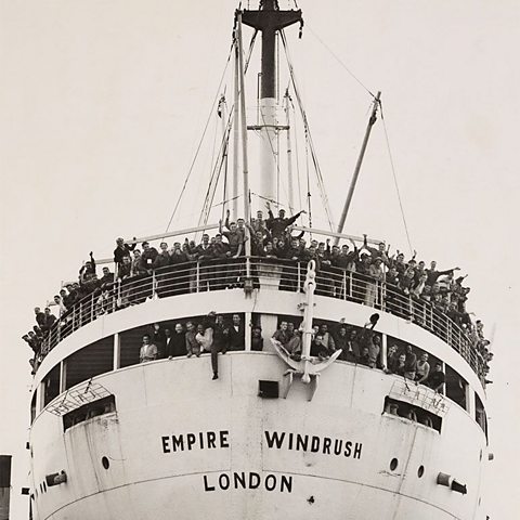 A black and white photograph of the Empire Windrush arriving in Britain on 21st June 1948. The decks are filled with people waving.