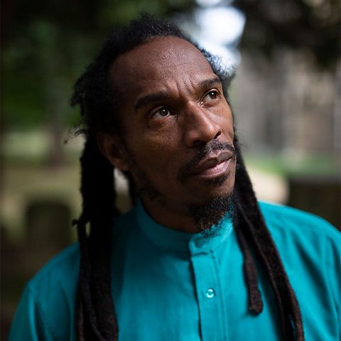 A portrait photograph of Benjamin Zephaniah. He is wearing a blue shirt and looking upwards.