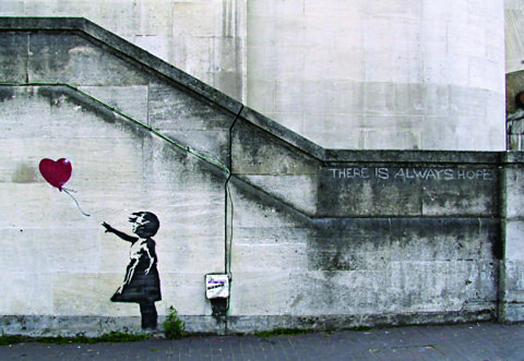 A spray painting on a wall of a girl reaching for a heart shaped balloon.