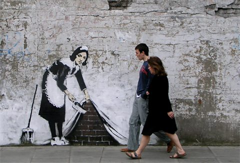 A spray painting on a wall of a maid holding a sweeping brush and lifting a piece of fabric up.