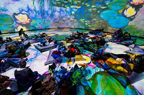 A group of people lying on the floor in a room full of projected colourful artwork.