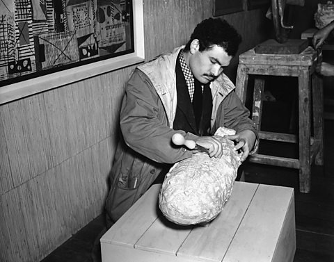 A black and white photo of Eduardo Paolozzi working on a sculpture.