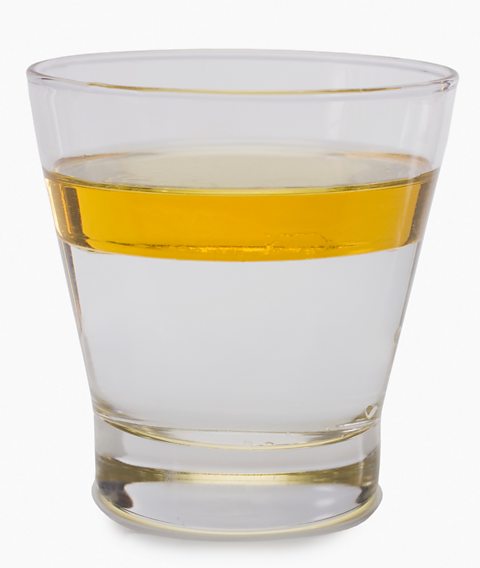 A glass containing oil and water demonstrating the different densities of the liquids.