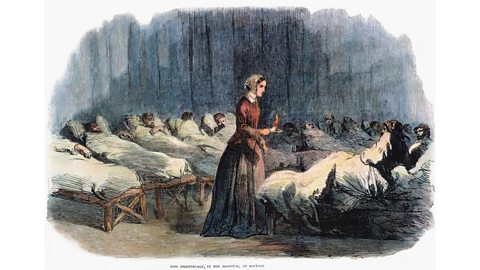 An illustration of Nightingale holding a lamp in the centre of a dark room full of soldiers, who are lying on wooden frame beds under sheets. A caption reads: 'Miss Nightingale, in the hospital, at Scutari'