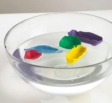 Boats made from modelling clay in a bowl of water.