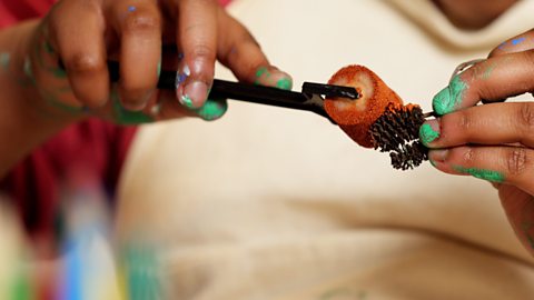 A girl is rolling some red printing paint over small pine cones