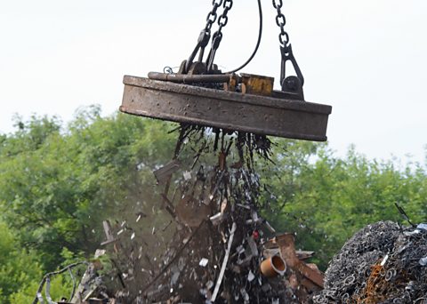 A large industrial magnet picking up metal at a scrap yard.