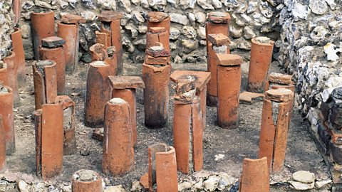 The ruins of a Roman underfloor heating system. Upright tubes made from orange pottery tile - filled with stone or tile - protrude from the ground.